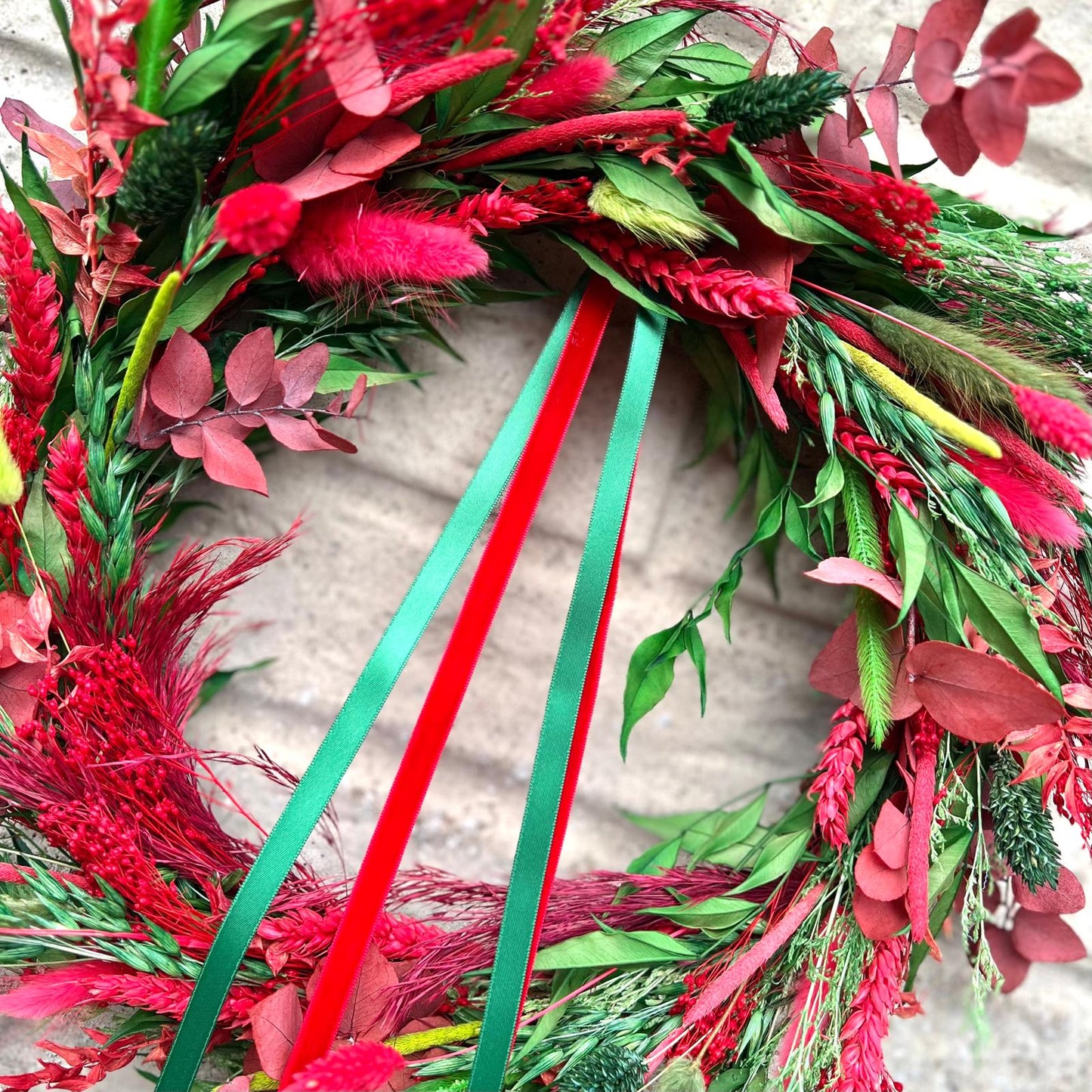 Decorative wreath with red and green feathers and ribbons on a neutral background