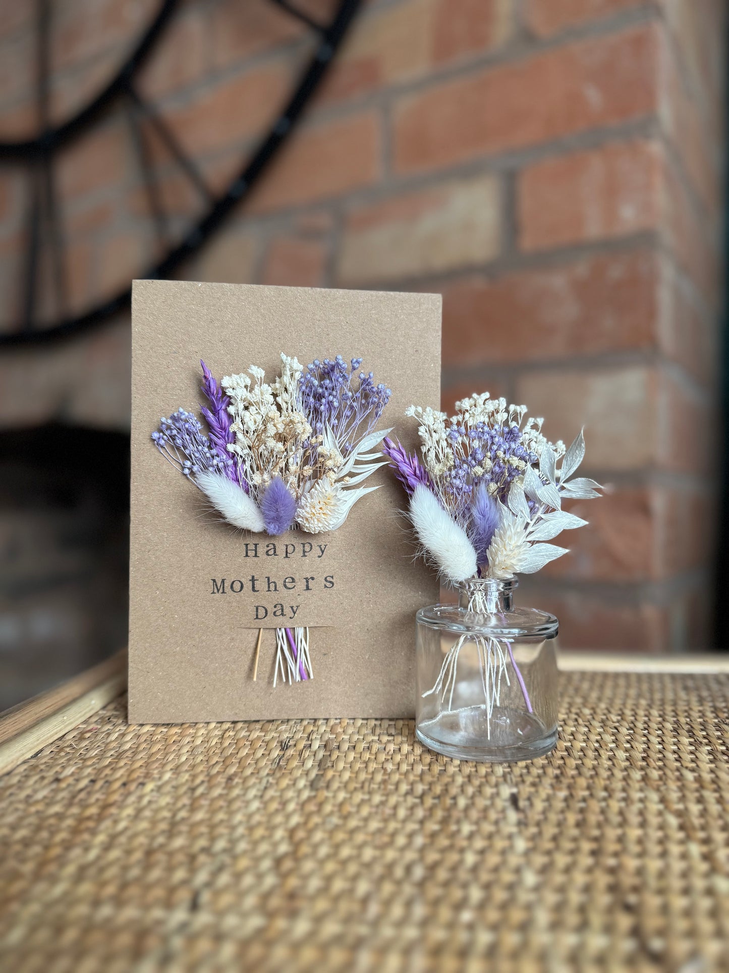 Dried flower card displayed on rattan shelf for mother day celebration. Small mini vase arrangement is displayed alongside the card to show it’s purpose