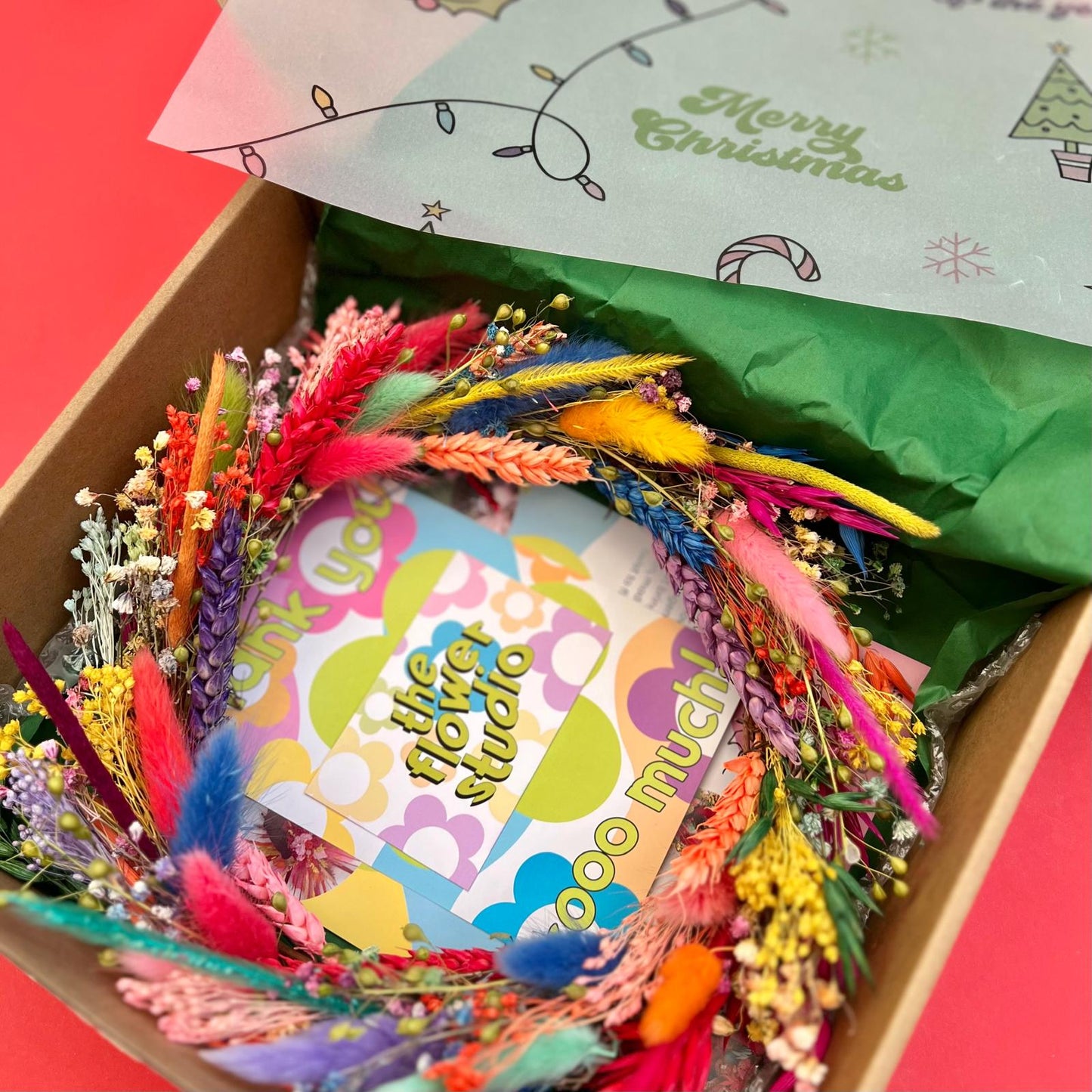 Colorful flower arrangement with a card inside a box, featuring a 'Merry Christmas' message on the paper.