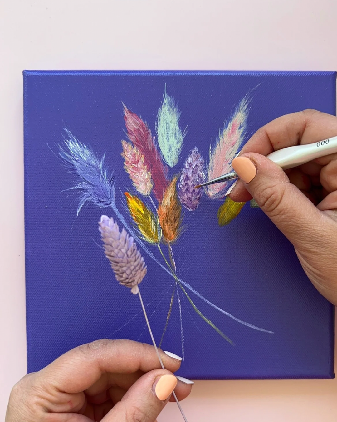 Person painting a floral design on a blue canvas with a paintbrush.