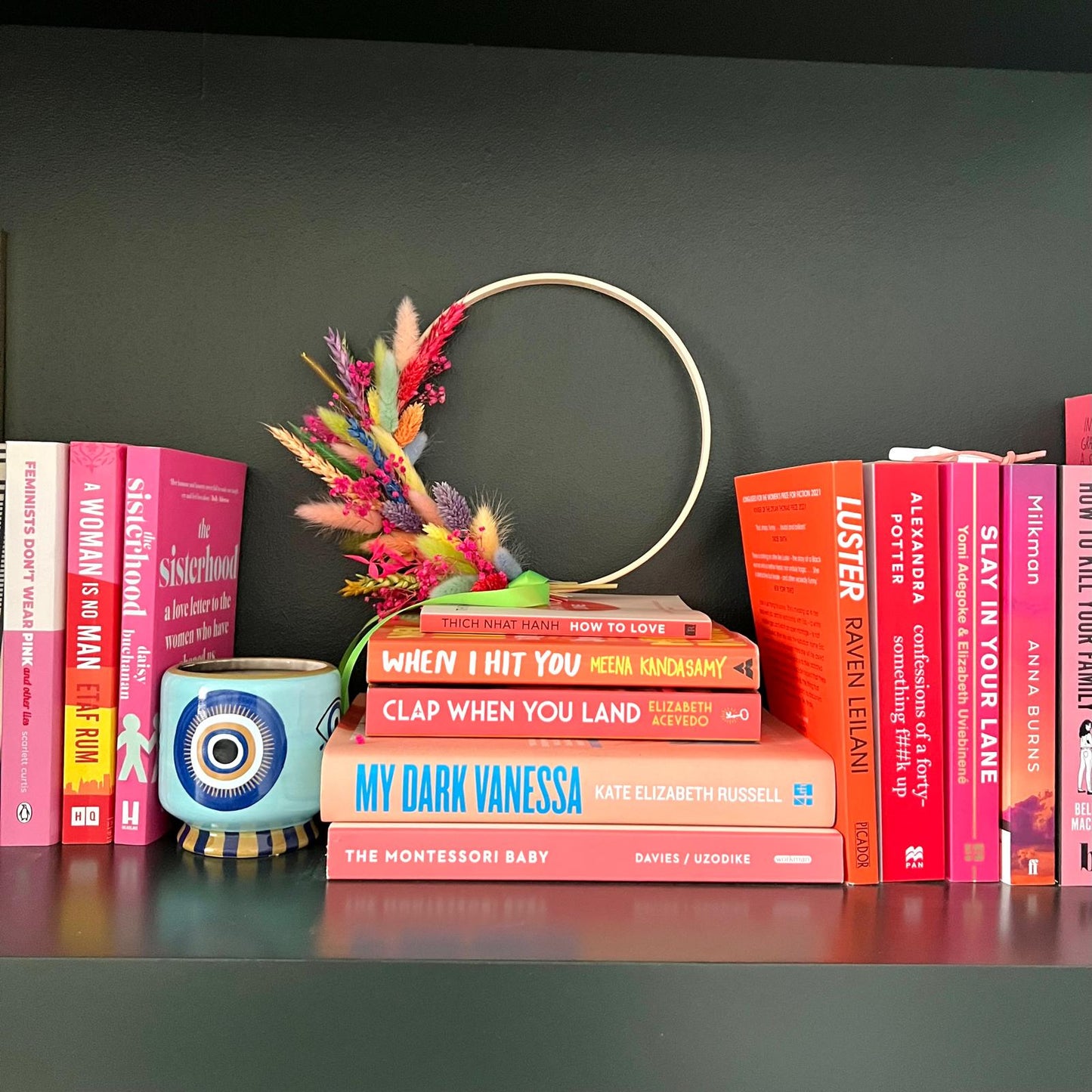 Vibrant mixed dried flower hoop featuring pink, orange, purple, and green textures on a minimal frame sitting on a stack of books with my dark vanessa from Kate Elizabeth Russell showing prominently