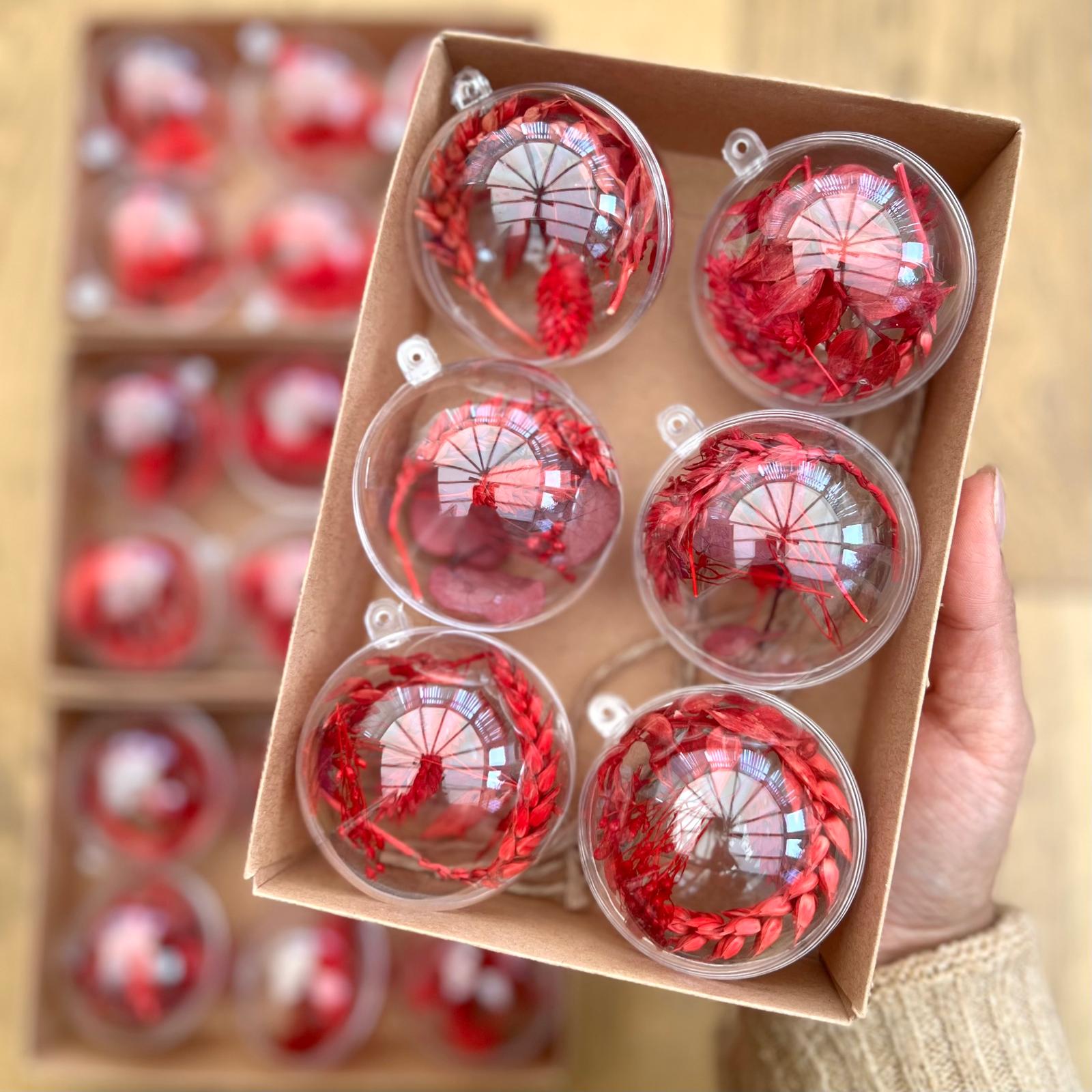 Set of red and clear Christmas ornaments in a box held by a hand.
