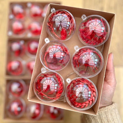 Set of red and clear Christmas ornaments in a box held by a hand.