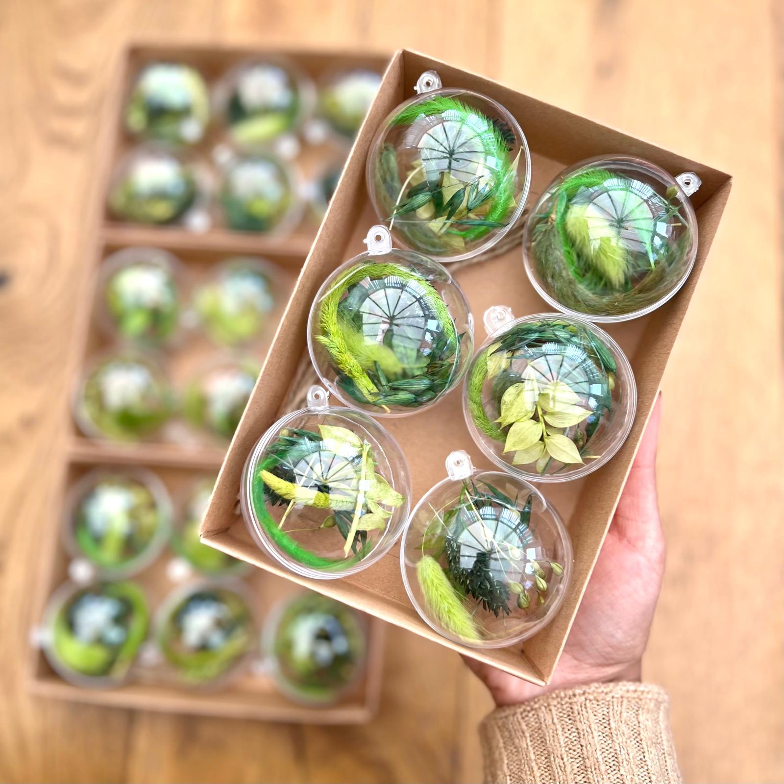 Clear spherical ornaments with greenery inside, displayed in a cardboard box on a wooden surface.