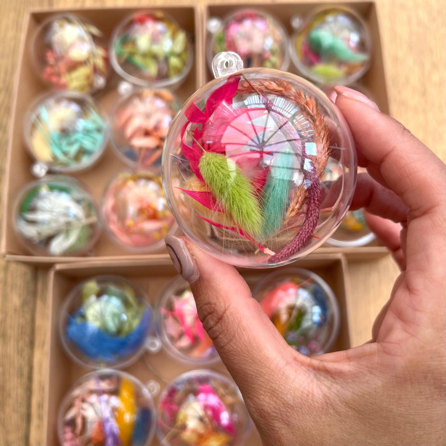 Hand holding a decorative item with colorful elements in front of a box of similar items.