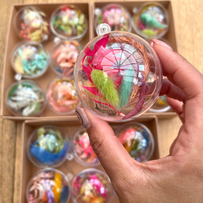 Hand holding a decorative item with colorful elements in front of a box of similar items.