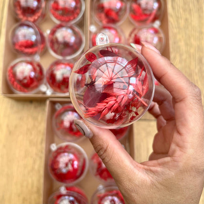 Hand holding a transparent sphere with red floral design, with a box of similar spheres in the background.