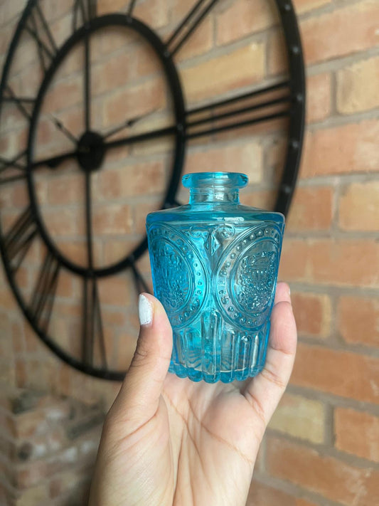 Blue glass bottle held in front of a brick wall with a decorative wheel.