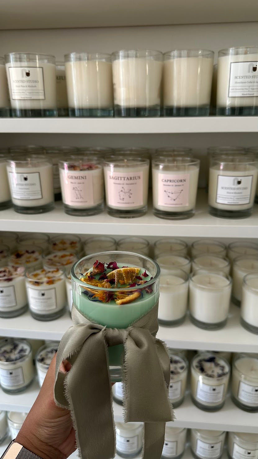Hand holding a jar of candle with shelves of similar jars in the background