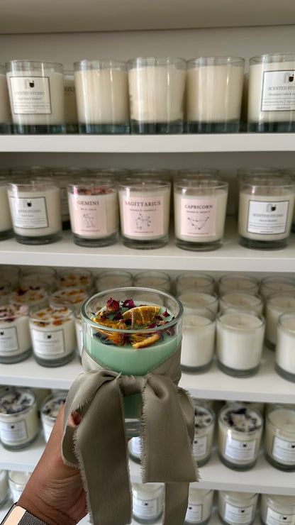 Hand holding a jar of candle with shelves of similar jars in the background
