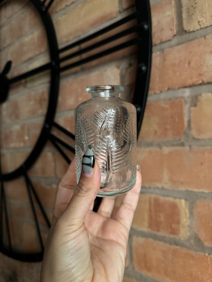 Hand holding a glass bottle with leaf patterns against a brick wall.