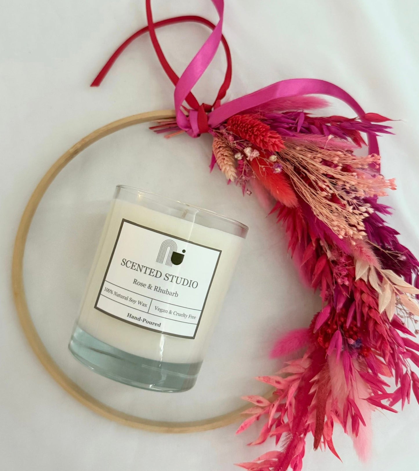 Candle in a glass jar with a decorative pink bow and floral arrangement on a white background