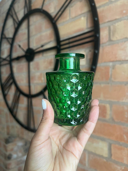 Green textured glass bottle held in front of a brick wall with a clock.