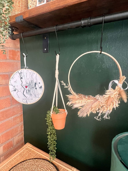 Rustic boho wreath made with soft dried flowers and natural textures, displayed against a green wall with a plant pot hanging and another wood hoop that has an embroider
