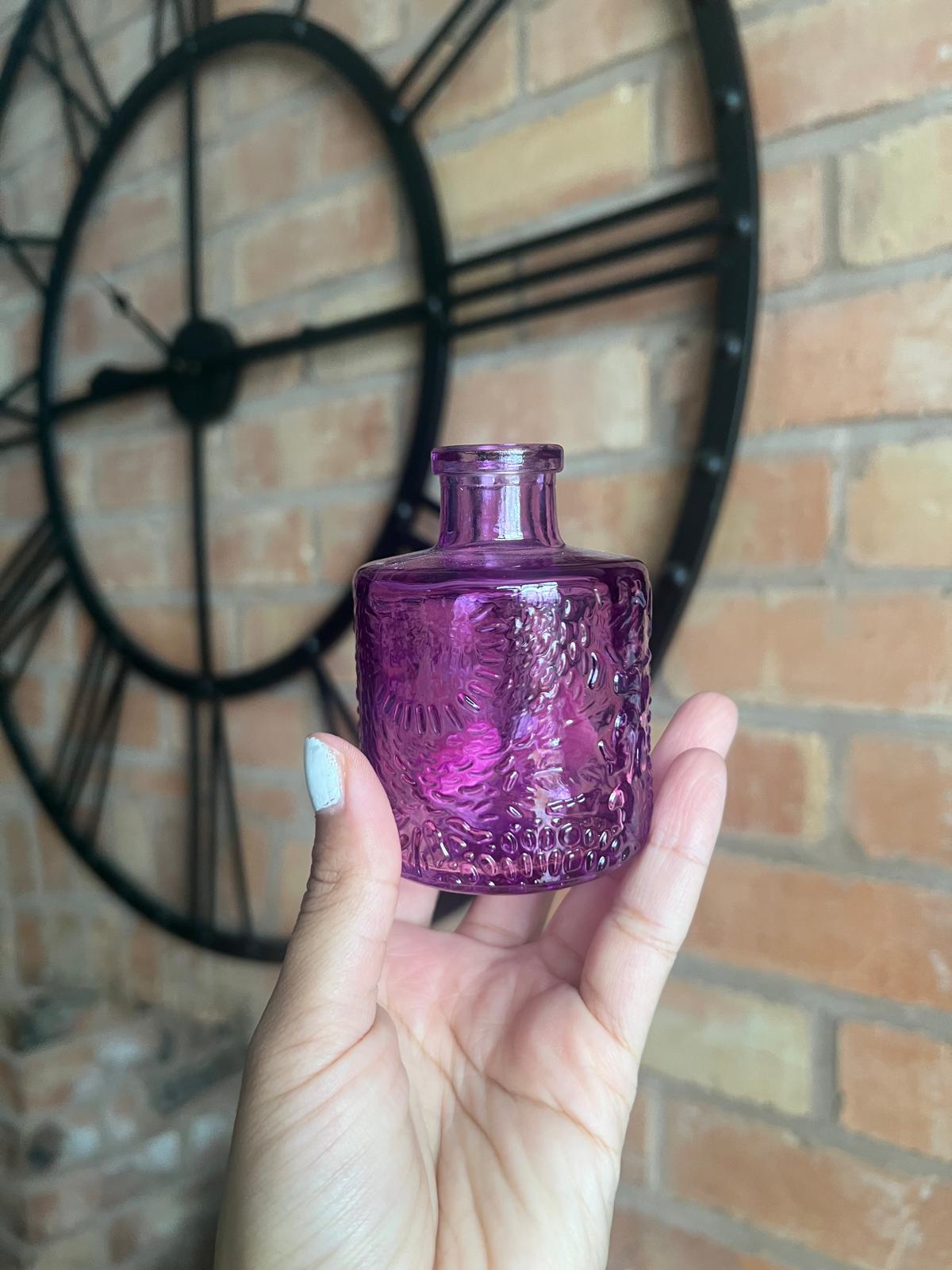 Hand holding a purple glass bottle against a brick wall background