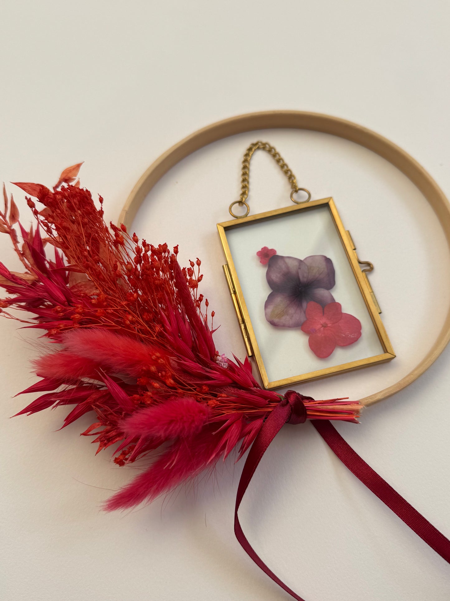 Decorative hoop with red feathers, a gold frame with flowers, and a purple flower on a light background