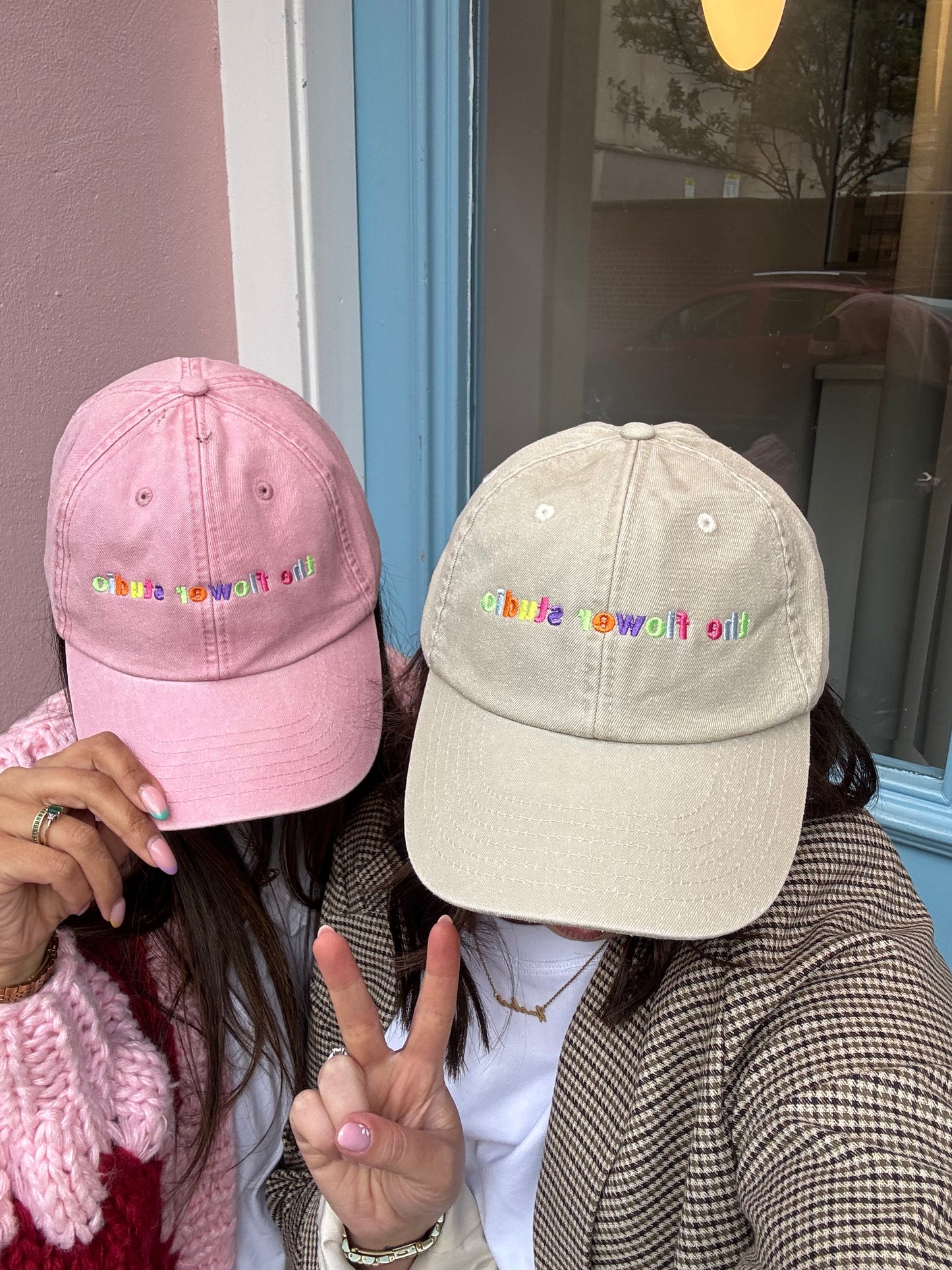 Two pink and beige baseball caps with colorful lettering held by a person.