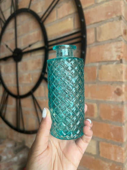Hand holding a textured teal glass bottle against a brick wall background