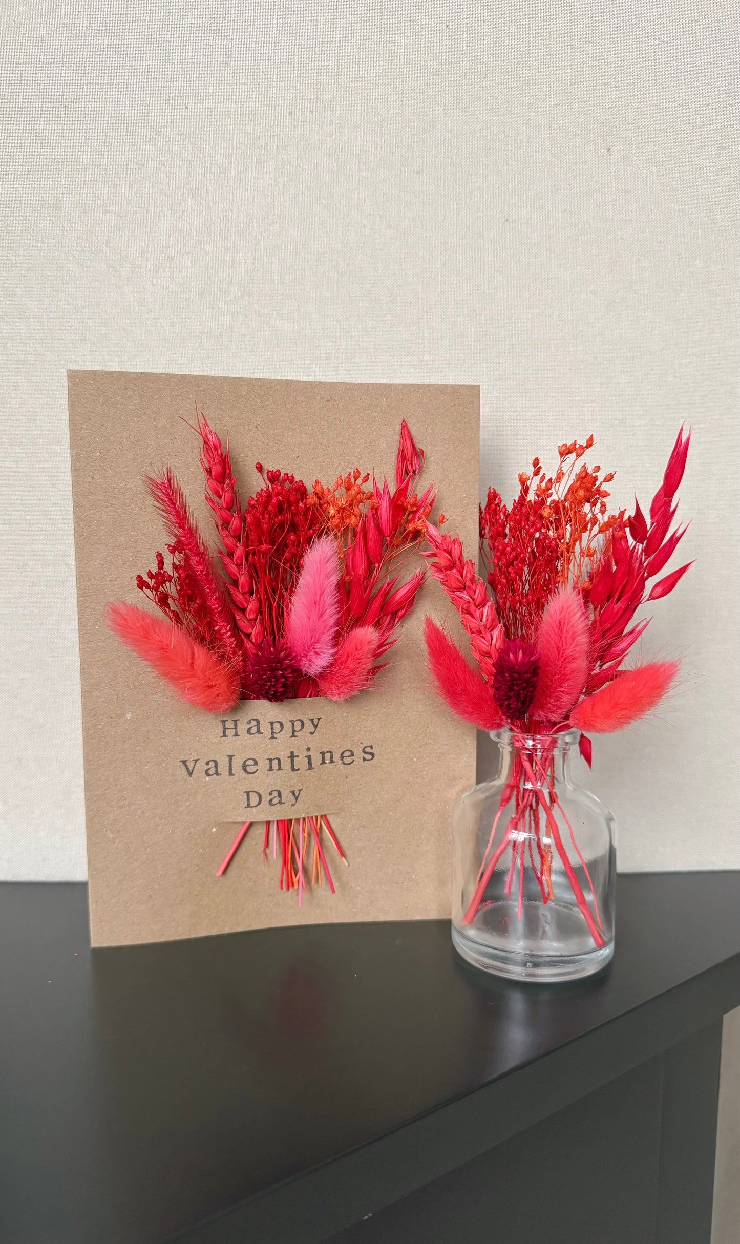 Valentine's Day card with red floral arrangement and a glass vase on a dark surface.