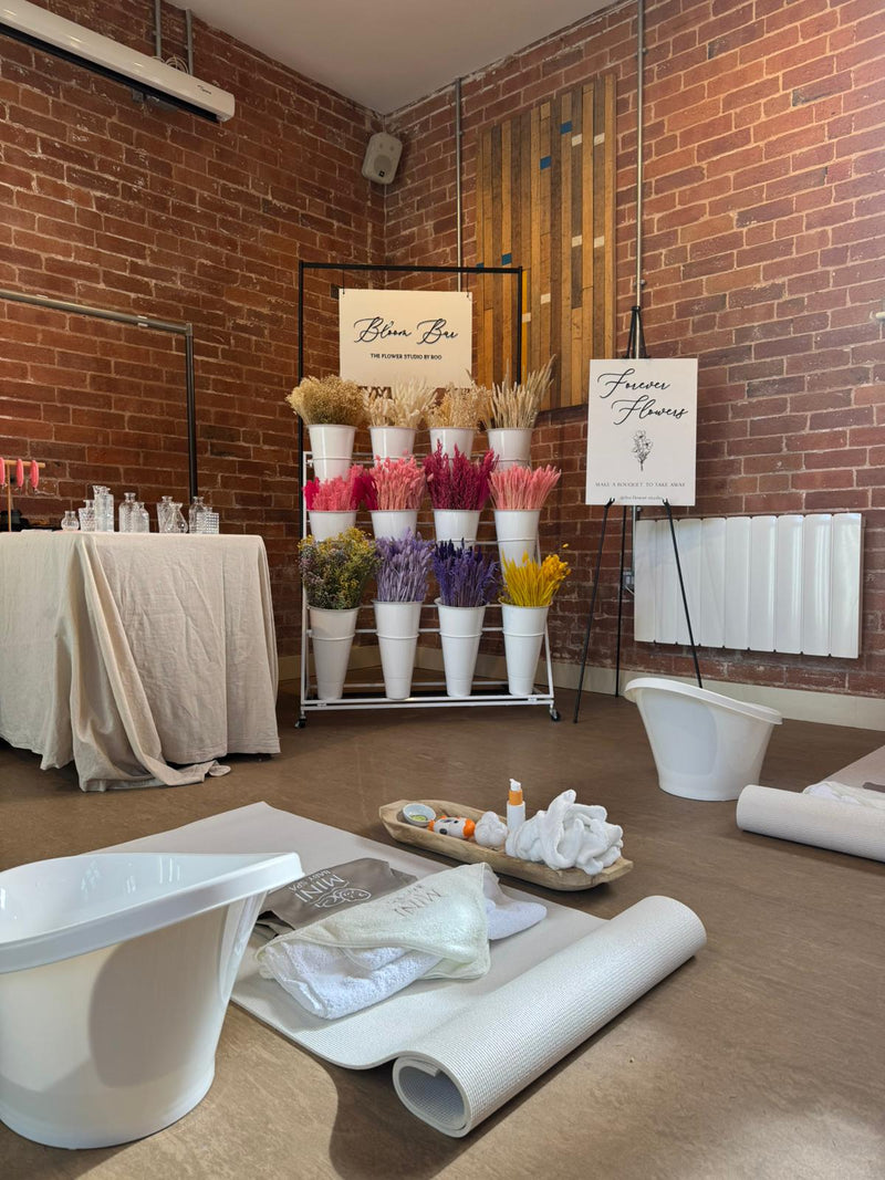 Floral arrangement display with 'Blume Box' branding in a room with brick walls and white furniture.