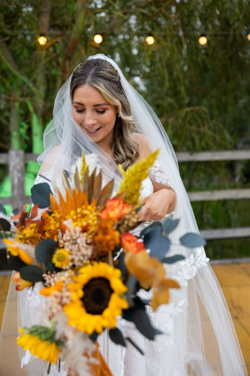Bride holding a bouquet of sunflowers and other flowers with a blurred background