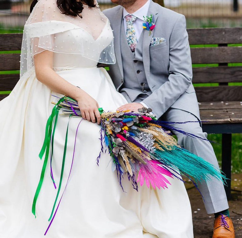 Couple in wedding attire sitting on a bench with a colorful bouquet.
