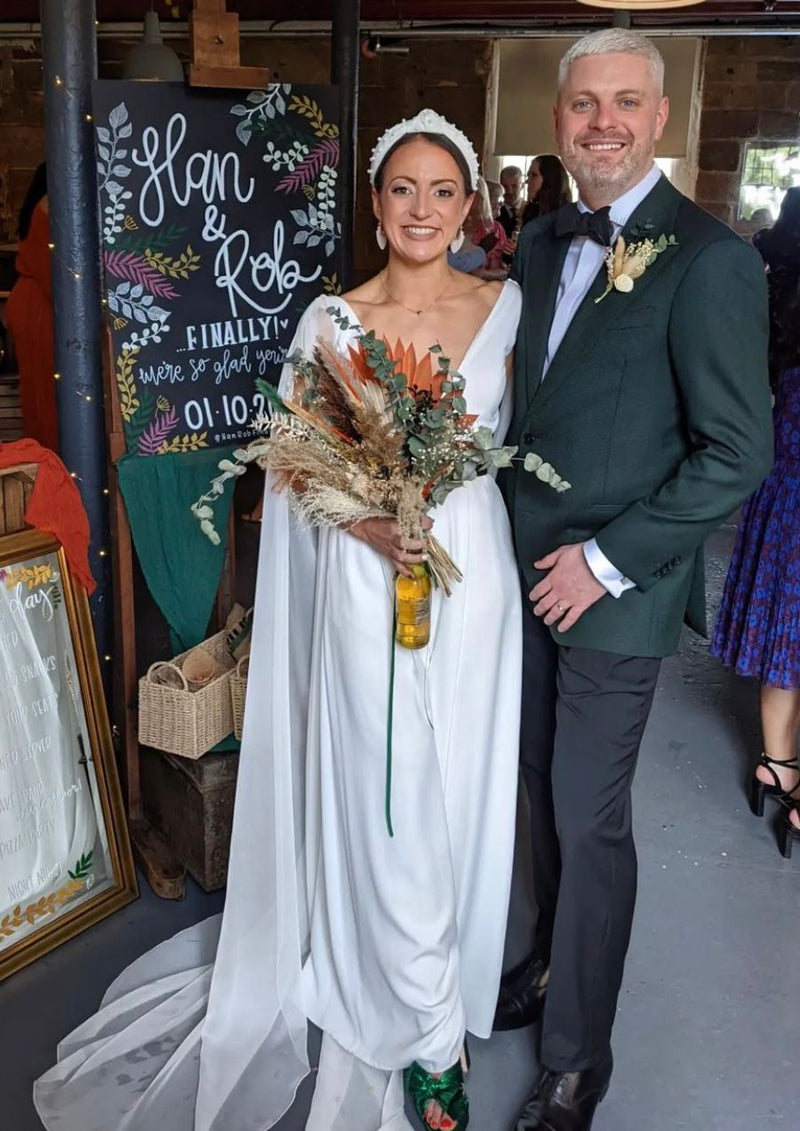 Couple in wedding attire standing together with a decorated backdrop
