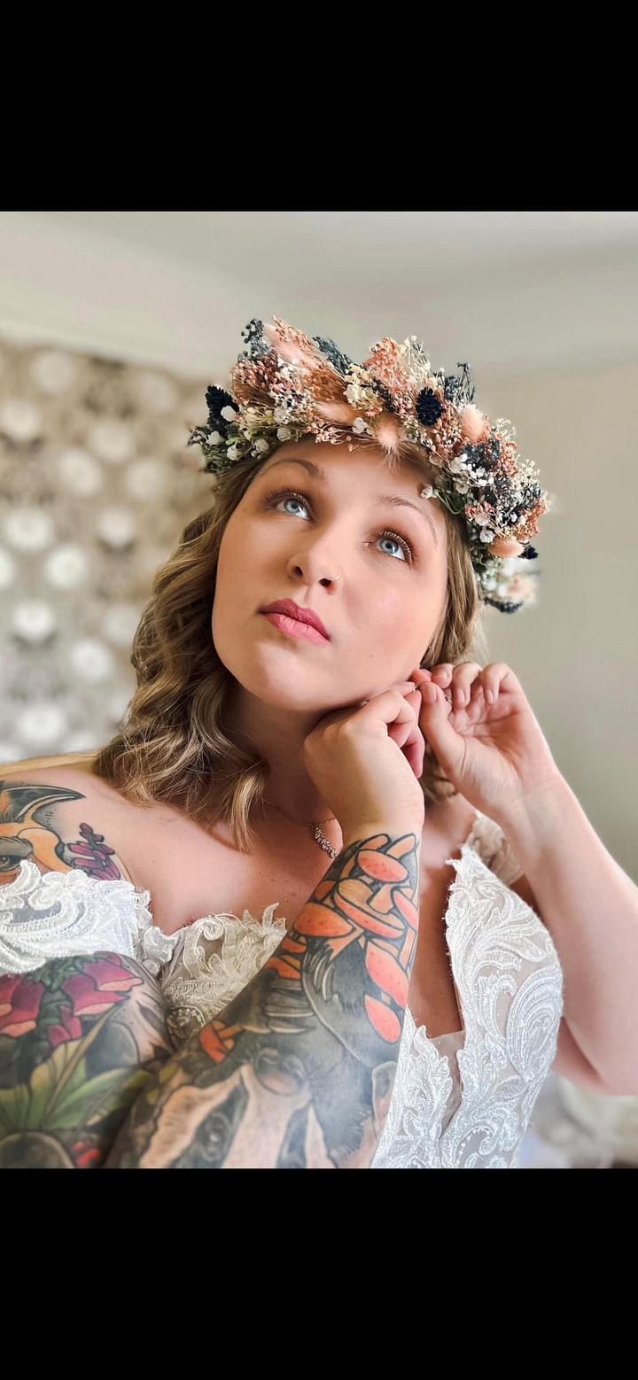 Woman wearing a floral crown and lace garment with tattoos, looking up.