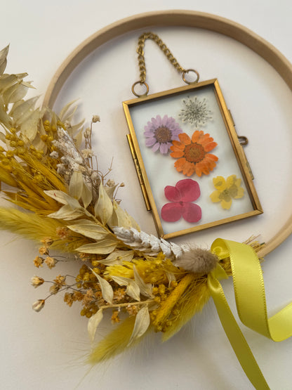 Decorative hoop with pressed flowers and a yellow ribbon on a light background