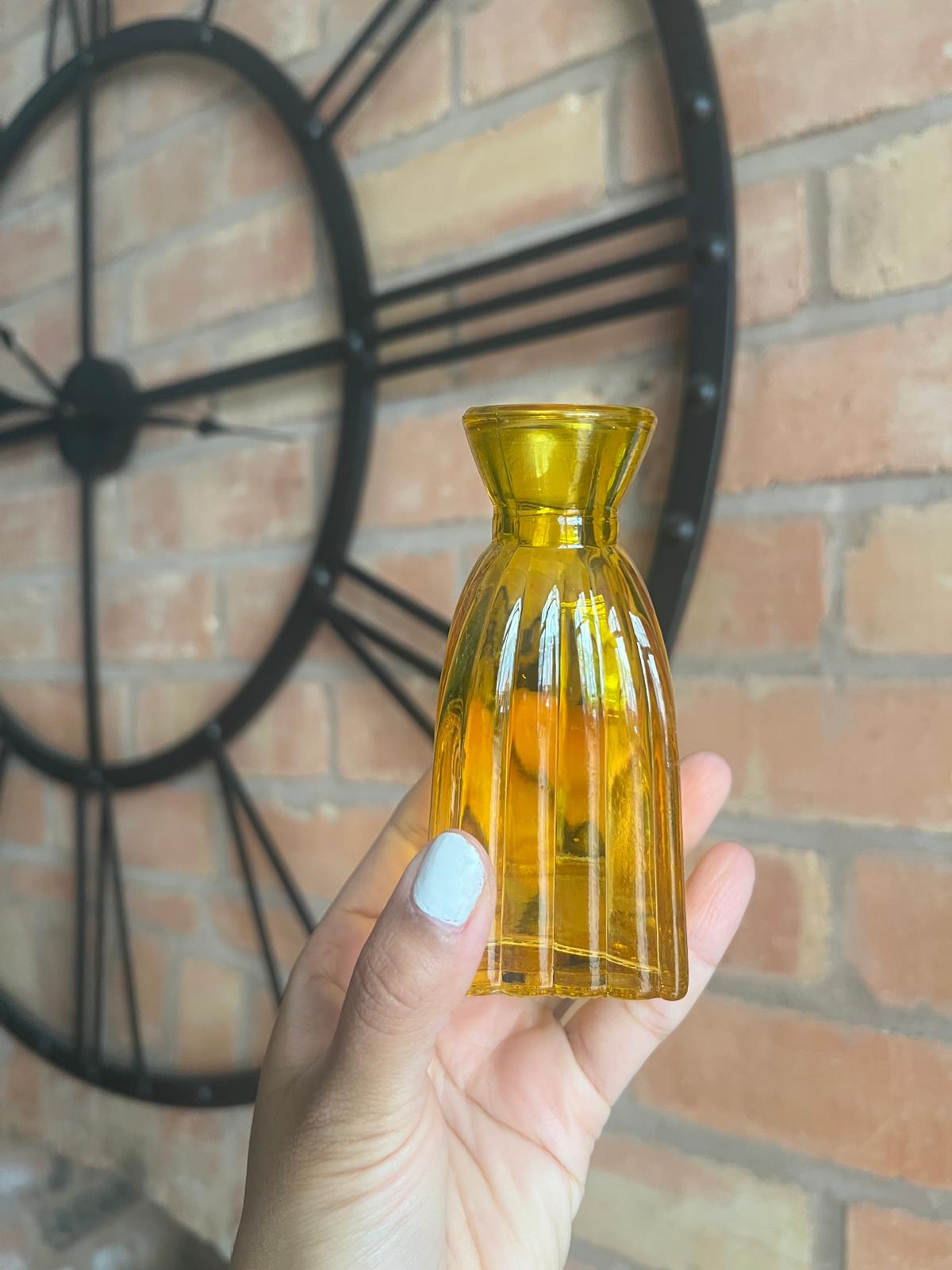 Hand holding a yellow bottle against a brick wall with a clock.