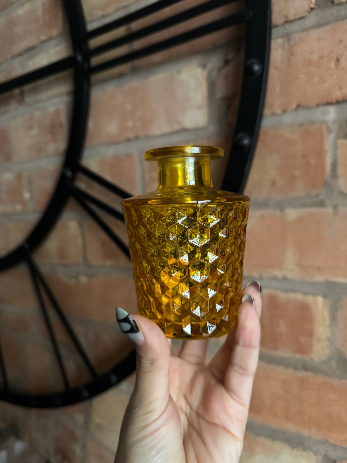 Hand holding a textured amber glass vase against a brick wall.