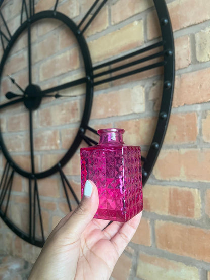 Hand holding a pink textured bottle against a brick wall with a clock.